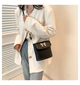 Dettaglio borsa a secchiello nera con fiocco argento indossata da modella in blazer