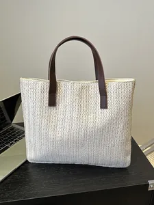 Detail of hand-woven straw tote with premium brown leather straps on a wooden desk