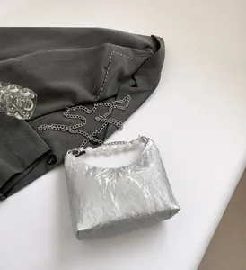 Dettaglio borsa a pieghe argento metallizzato con manico di perle e logo su un blazer
