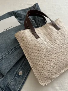 Detailed close-up of woven straw tote bag texture and brown reinforced handle straps