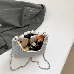 Vista interna della borsa argentata con perle con smartphone, rossetto e profumo