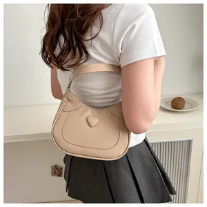 Detail showing the creamy beige crescent moon bag featuring a 3D heart-shaped buckle design