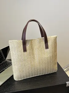 Detailed close-up of woven straw tote bag with brown leather handles on wooden desk