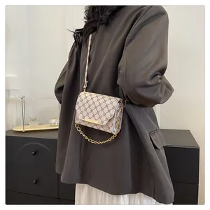 Detail of vintage patterned crossbody bag with gold chain strap on a model shoulder