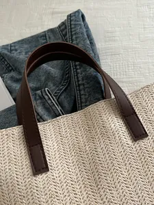 Close-up of cream woven tote bag with herringbone pattern and dark brown faux leather handle