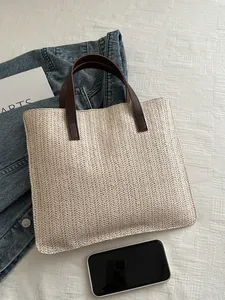 Flat lay of a woven straw tote bag with brown leather handles and denim jacket accents