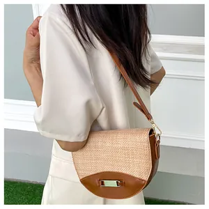 Detail of woven straw and brown leather saddle bag with gold buckle on a model