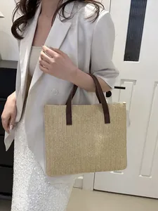 Detailed view of beige straw tote bag with brown leather handles and herringbone weave