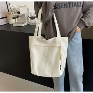 Detail of a creamy white canvas tote bag featuring a front zipper pocket and fashion tag