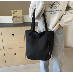 Detail of black canvas tote bag showing side zipper pocket with woven puller detail