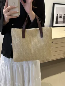 Detail of herringbone straw weave texture and brown faux leather handles on a summer tote
