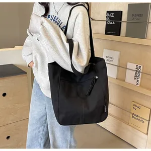 Detail of black canvas tote bag showing side zipper pocket and fashion label on shoulder strap