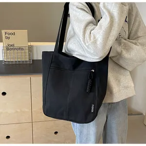 Detail view of black canvas tote bag showing zipper pocket and FASHION woven label detail