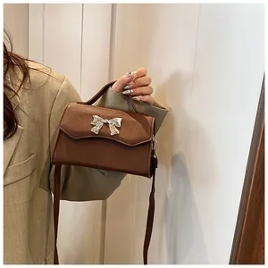 Dettaglio borsa marrone in pelle PU con patta ondulata e fibbia metallica a fiocco