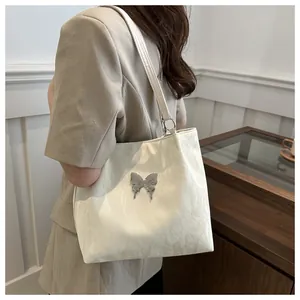 Detail of cream-white underarm bag with silver butterfly metal ornament and pleated texture