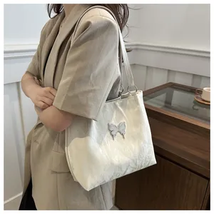 Detail of cream-colored tote bag featuring 3D silver butterfly and pleated texture
