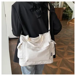 Detail of a large off-white canvas tote bag with front buckle pocket and side pocket straps
