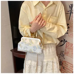 Detalle de bolso vintage en forma de concha con bordado de mariposas y asa de metal oro