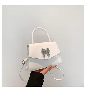 Close-up of white patent leather handbag featuring a silver metallic butterfly buckle