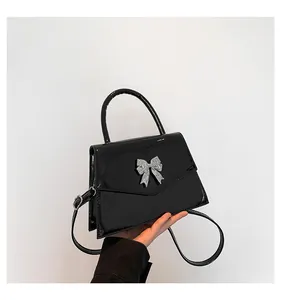 Close-up of a glossy black patent leather handbag with a silver butterfly metal clasp