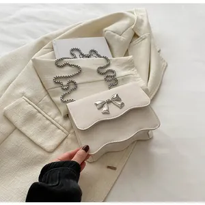 Detail of cream shoulder bag with wave edges and silver metallic bow buckle accent