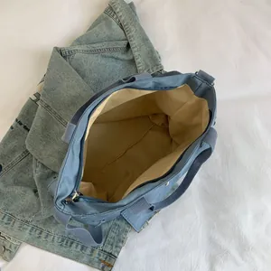Blue canvas tote bag with zipper closure and wide shoulder strap on denim background