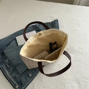 Large straw tote bag with brown leather handles and magnetic closure on denim background