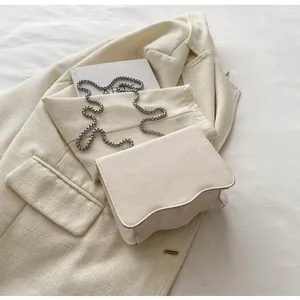 Close-up of cream white chain bag with wave-cut edges on a chic neutral background