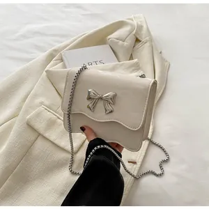 Macro detail of creamy white bag with wave edge flap and silver metal bow buckle