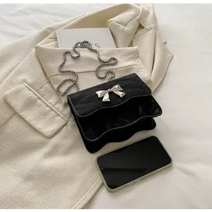 Detail of a black wrinkled patent leather crossbody bag with a silver bow and bead chain