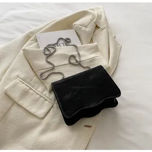 Detail of black wave-edge crossbody bag with silver chain on white blazer