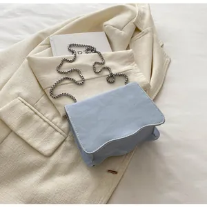 Detail of light blue faux suede bag with wavy edges and silver ball chain on a blazer
