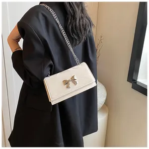 Détail d'un sac bandoulière blanc crème avec boucle nœud argentée et chaîne sur un modèle
