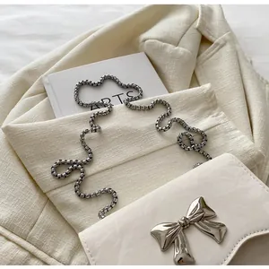 Detail of cream flap bag featuring a silver metal bow buckle and elegant snake chain strap