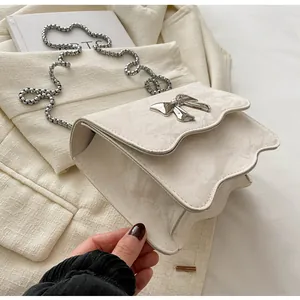 Close-up of cream white wavy crossbody bag with silver bow accent and metal chain strap