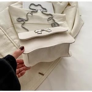 Close-up of beige chain bag showing wavy leather texture and silver bow buckle detail