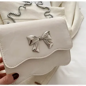 Detailed view of cream PU crossbody bag with silver bow buckle and wavy flap edge