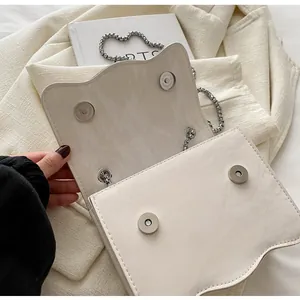 Detailed close-up of textured beige shoulder bag with double magnetic snaps and silver chain