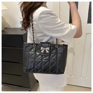 Detail of black quilted shoulder bag featuring silver bow buckle and chain strap