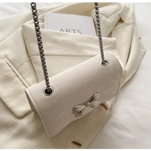 Close-up of cream shoulder bag with silver bow clasp and elegant marble texture leather