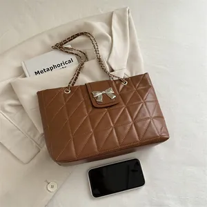 Brown quilted shoulder bag with silver bow buckle and chain strap on neutral background
