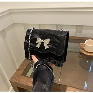 Detail of black pleated crossbody bag featuring a silver metal bow and chain strap