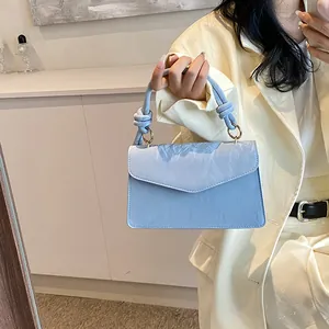 Sac à main bleu clair plissé avec poignée nouée et détails dorés porté par un mannequin