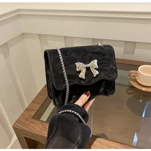 Detailed view of black textured mini crossbody bag with silver bow and wave edge lid