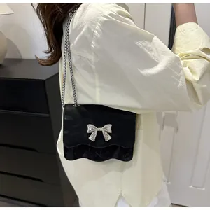 Detail shot of a black wave-edge crossbody bag with silver bow and chain strap