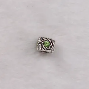 Detailed close-up of a square silver charm bead featuring rose relief and a green crystal