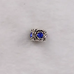 Macro detail of silver rose flower charm bead with a deep blue crystal center