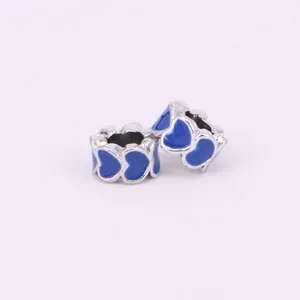 Detail of two silver DIY charms with heart-shaped blue enamel patterns on white background