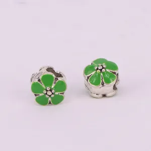Macro shot of two green enamel cherry blossom charms with large holes in silver metal