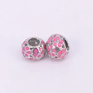 Detail showing two silver beads with pink enamel heart patterns and hollow-out design